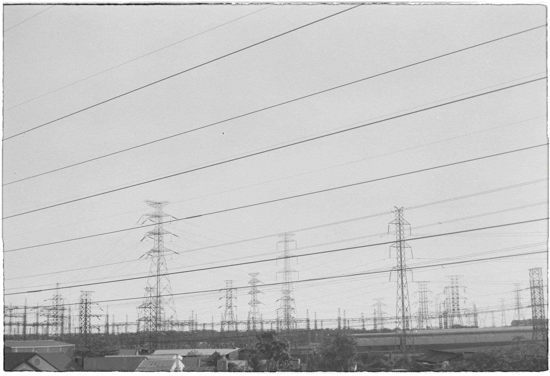 Monochrome image of rows of power lines and pylons in an industrial zone.