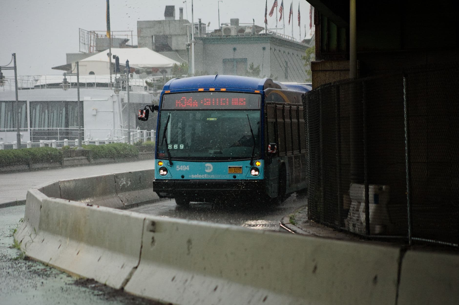 City bus navigating wet urban streets amidst heavy rain, showcasing public transportation in action.